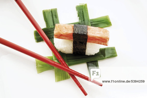 Sushi Nigiri  made with imitation crab meat and rice wrapped in nori seaweed and placed beside red chopsticks on interwoven leek strips