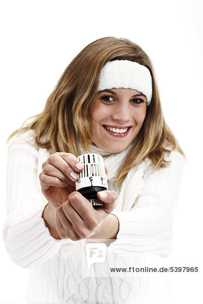 Junge Frau im weißen Rollkragenpullover mit Stirnband hält Heizungsthermostat