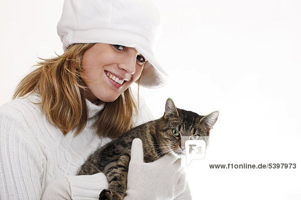 Junge Frau im weißen Rollkragenpullover mit Wollmütze hält Katze