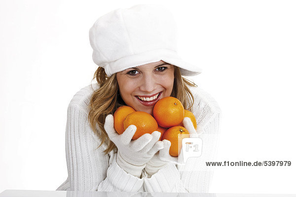 Young woman in a white turtleneck sweater with woolen hat holding oranges