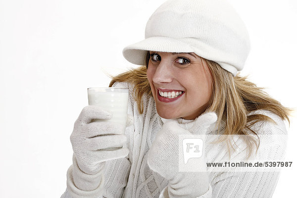 Young woman in a white turtleneck sweater with woolen hat holding a glass of milk