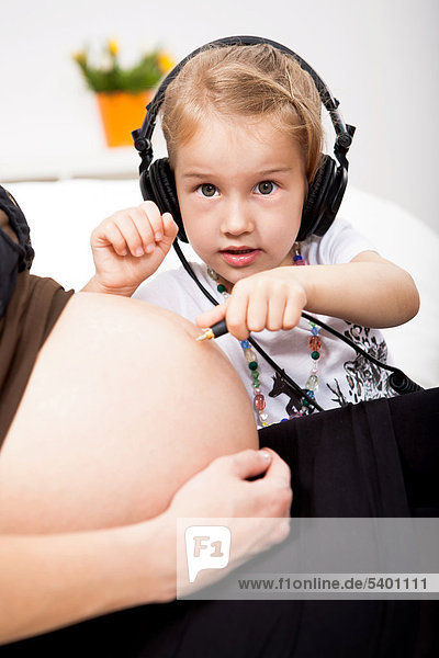 Mädchen mit Kopfhörer hört am Bauch ihrer schwangeren Mutter