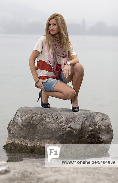 Junge blonde Frau in Hotpants posiert auf Stein im Wasser