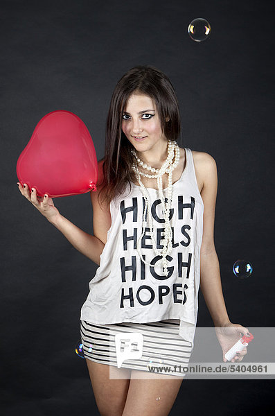'Young woman  wearing a top with the words ''High heels  high hopes''  with bubbles and a heart-shaped balloon'