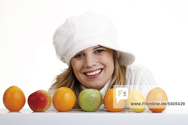 Young woman wearing a white jumper and a hat behind apples  oranges and a lemon