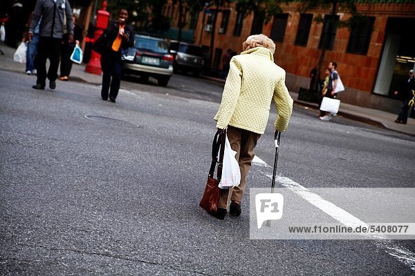 Elderly Woman with a cane and shopping bag  crossing a busy street