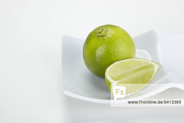 Limette (Citrus latifolia) und Limettenstück auf einem weißen Teller