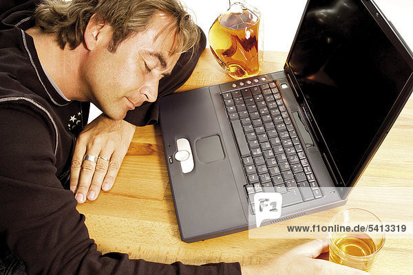 Man sleeping in front of a laptop next to a bottle of whiskey