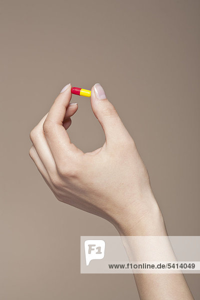 Hand einer jungen Frau hält eine Pille  Kapsel zwischen den Fingern