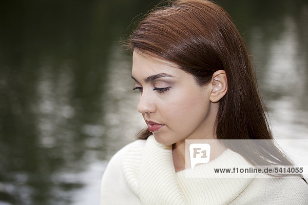 Young woman looking thoughtful  lowered eyes  in front of a lake