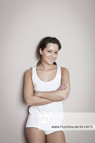 Young woman with a friendly smile  wearing underwear  crossed arms  leaning against a wall