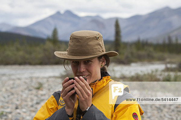 Junge Frau trinkt  genießt eine Tasse Tee  Wind River  Peel Watershed  hinten die nördlichen Mackenzie Mountains  Yukon Territory  Kanada