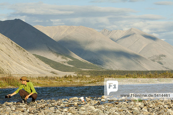 Young woman washing dishes in a river  camping  gravel bar  Mackenzie Mountains behind  Wind River  Peel Watershed  Yukon Territory  Canada