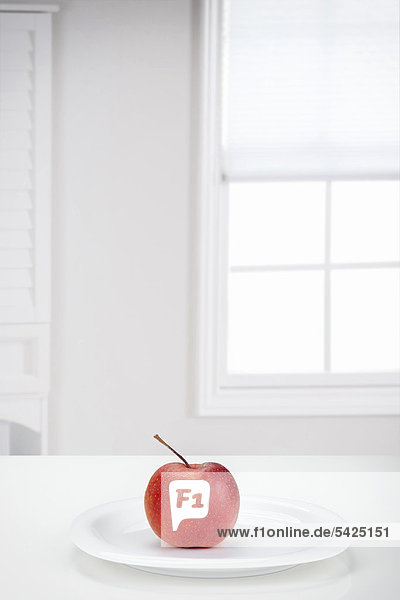 Roter Apfel (Malus domestica) der Sorte Boskoop auf einem weißen Teller vor einem Fenster