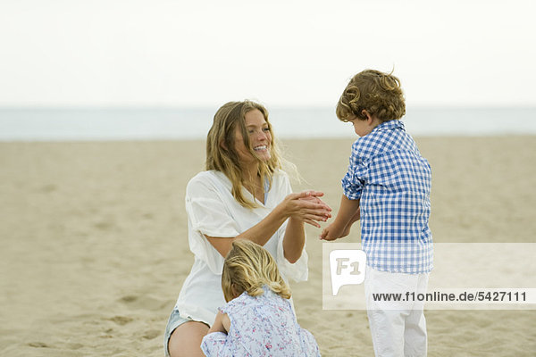 Mutter und Kinder spielen im Klang am Strand