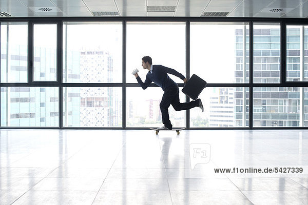 Businessman skateboarding with cup and briefcase in hands