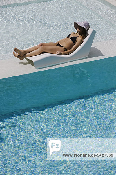 Junge Frau mit Sonnenhut auf dem Liegestuhl am Pool
