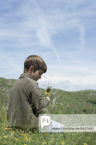 Junge kniend auf der Wiese mit Blumen in der Hand