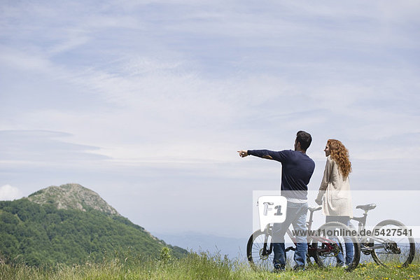 Ein Paar steht neben Mountainbikes und genießt die Aussicht auf die Berge.