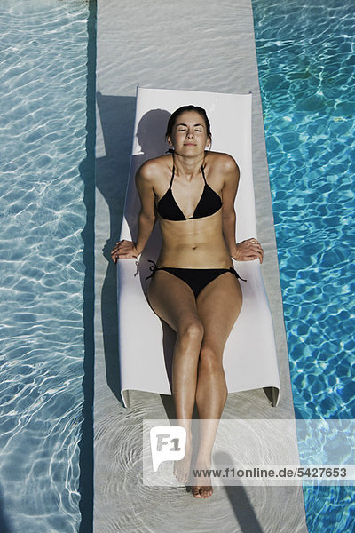 Young woman sunbathing on deckchair by pool