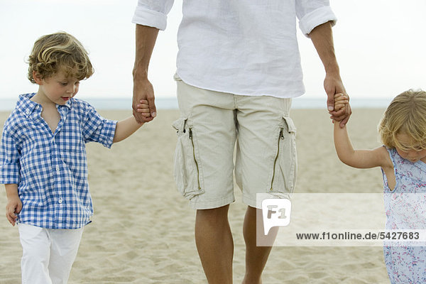 Vater und Kinder gehen Hand in Hand am Strand  abgeschnitten