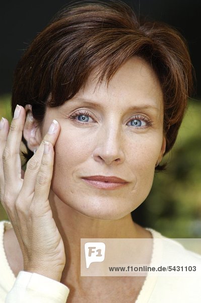 Portrait einer Frauen im mittleren Alter die sich mit Ringfinger Creme in die Augenfältchen klopft mund