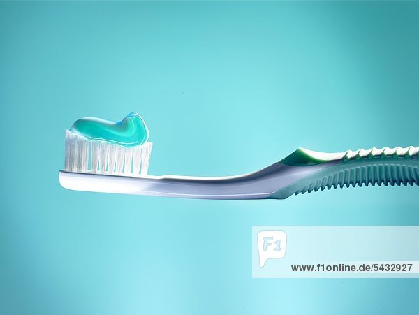 Zahnbürste mit türkis Zahnpasta vor blauem Hintergrund.