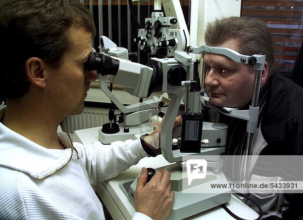 Augenarzt-Praxis : Der Arzt untersucht mit der Spaltlampe die Augen eines Patienten -