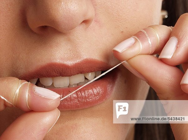 Frau  dunkle Haare  20-25 Jahre alt hält Zahnseide vor Ihren Mund mund