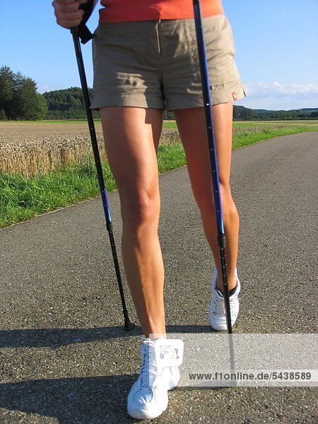 Frauenbeine beim Nordic Walking auf einem Feldweg.
