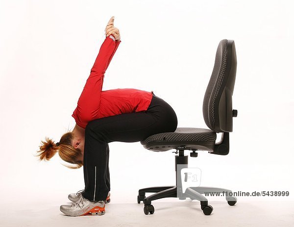 fit im Büro - junge Frau sitzt auf Bürostuhl und macht Gymnastik - Oberkörper auf Oberschenkel und Arme nach hinten oben nehmen - Beweglichkeit