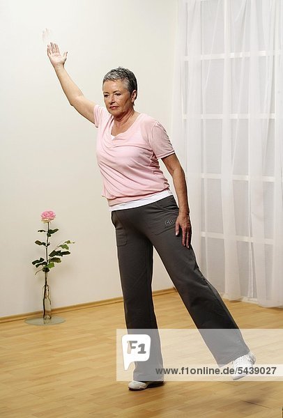 ältere Frau macht Gymnastik - Balance - Seniorin - Einbeinstand - Stand auf einem Bein - ein Arm diagonal über Kopf - Marionette