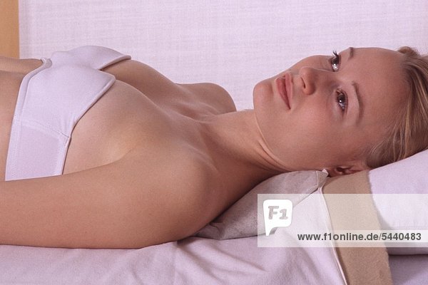 Junge Frau mit einem im Nackenbereich angelegten Heublumensack zur Behandlung von Muskulatur-Verspannungen