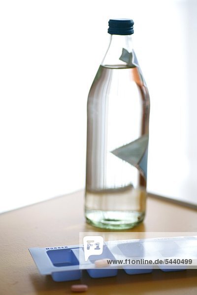 eine Flasche mit Wasser und Tabletten Tagesaufteilung - Dosierer - auf einem Nachttisch