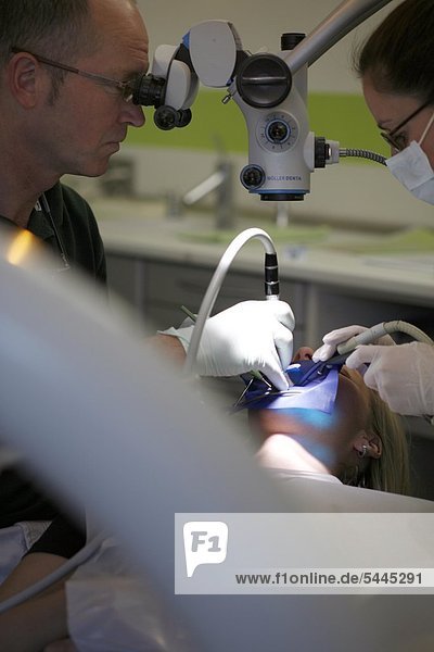 Zahnarztpraxis : Ein Zahnarzt und seine Zahnarzthelferin behandeln eine Patientin mit Bohrer und Absauger.