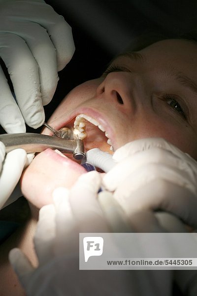 dental practice : a dentist and his dental assistant treat a female patient with a drill   a suction extractor and an inspection mirror