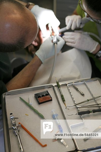 Zahnarztpraxis : Zahnarzt und Zahnarzthelferin behandeln eine Patientin mit Bohrer und Absauger