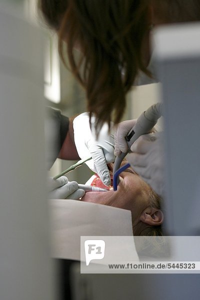 Zahnarztpraxis : Zahnarzt und Zahnarzthelferin behandeln Patienten mit Bohrer   Mundspiegel und Absauger