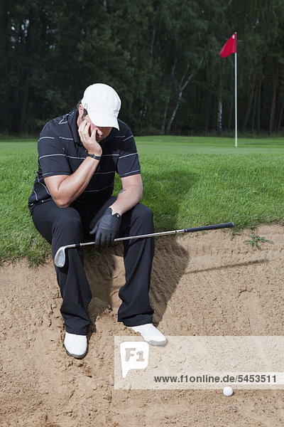 Ein unglücklicher Golfer sitzt am Rande einer Sandfalle.