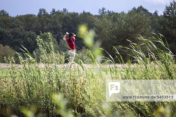 Eine Golfspielerin beim Abschlag  Fokus auf den Hintergrund