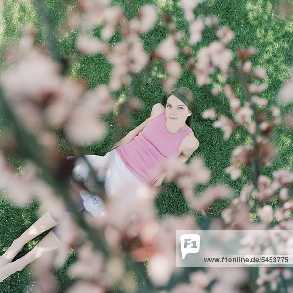 Ein auf Gras liegendes Mädchen schaut auf Kirschblüten.