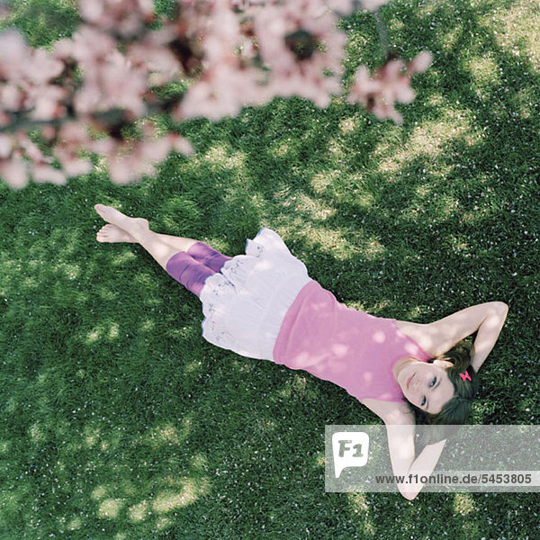 Ein Teenager-Mädchen im Gras liegend mit Händen hinter dem Kopf  aufblickend