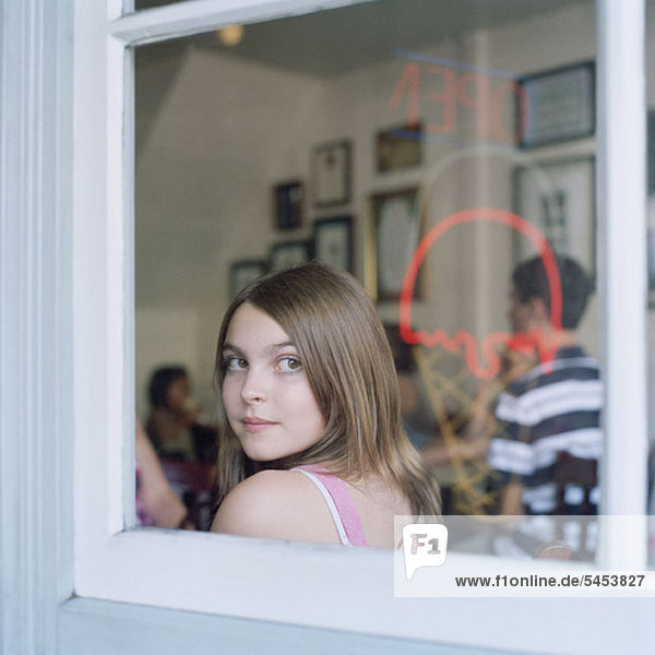 Ein Teenager-Mädchen  das durch ein Café-Fenster schaut.