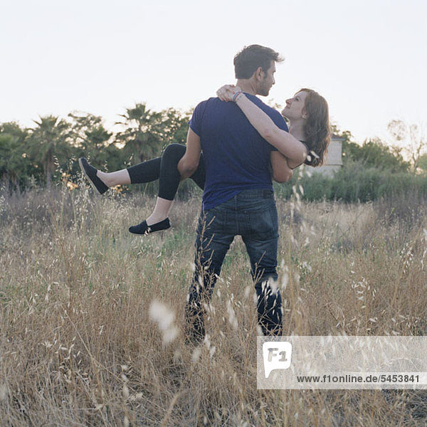 A young man carrying his girlfriend through a field