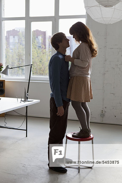 A young woman standing on a stool facing her tall boyfriend