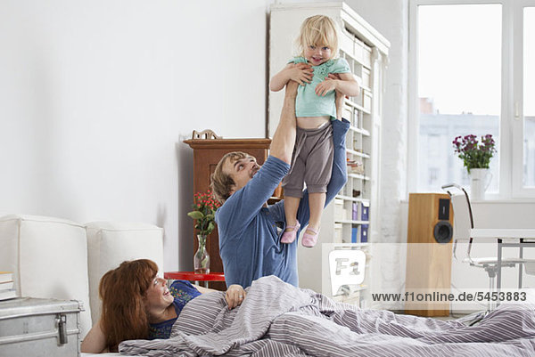 A couple in bed  man holding daughter aloft