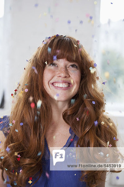 A smiling woman looking up at confetti falling