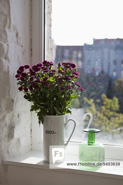 A green bottle and bouquet of flowers on a window sill