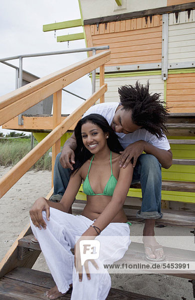 Ein junges glückliches Paar sitzt auf einer Treppe am Strand.