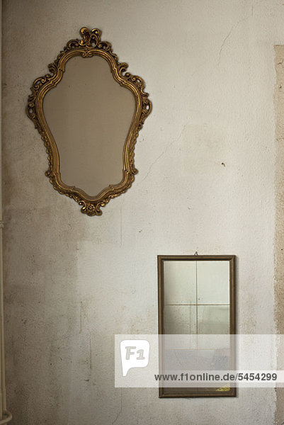 Zwei alte Spiegel  die an der nackten Wand hängen.